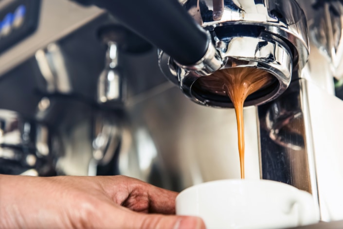 Close up of thai coffee being brewed by the machine flowing through portafilter into the cup at cafe