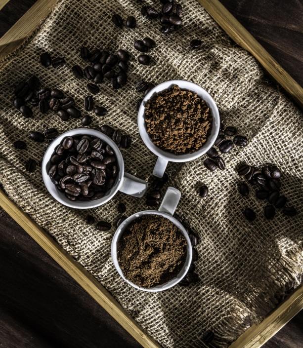 Three cups with Espresso, Cappuccino and Macchiato coffee with roasted raw coffee beans on wooden tray